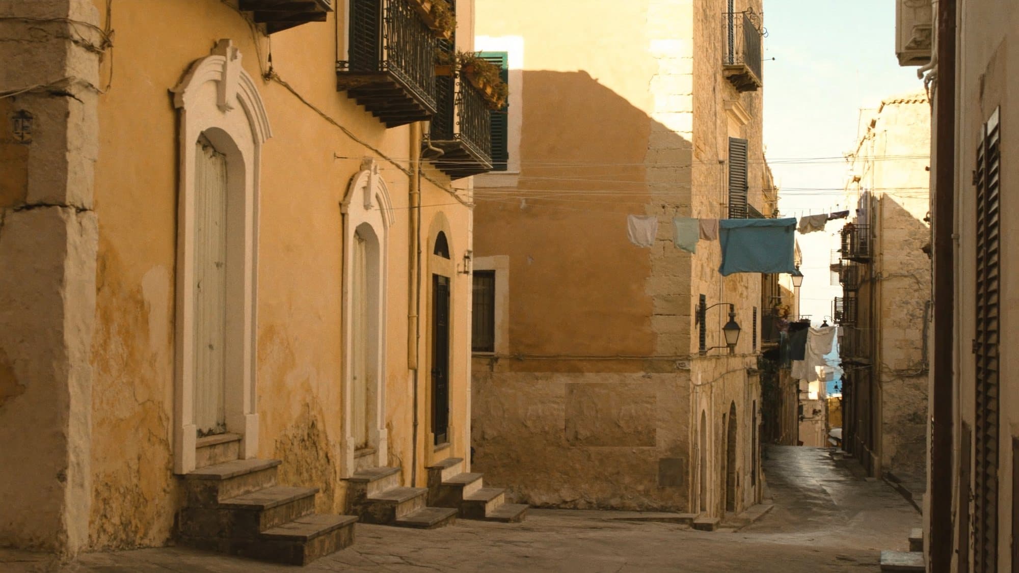 Ruelle d’un village sicilien aux façades ocre, escaliers de pierre et linge aux balcons