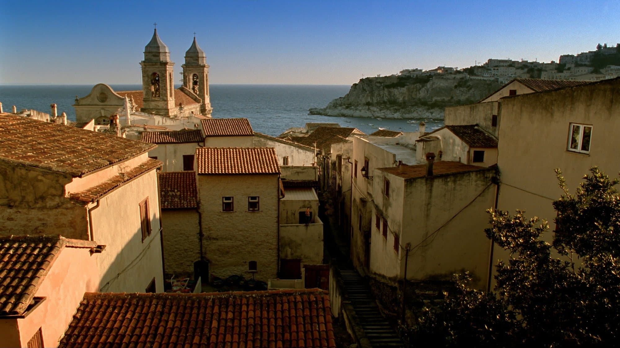 Village côtier sicilien au coucher du soleil, toits de tuiles et clocher face à la mer